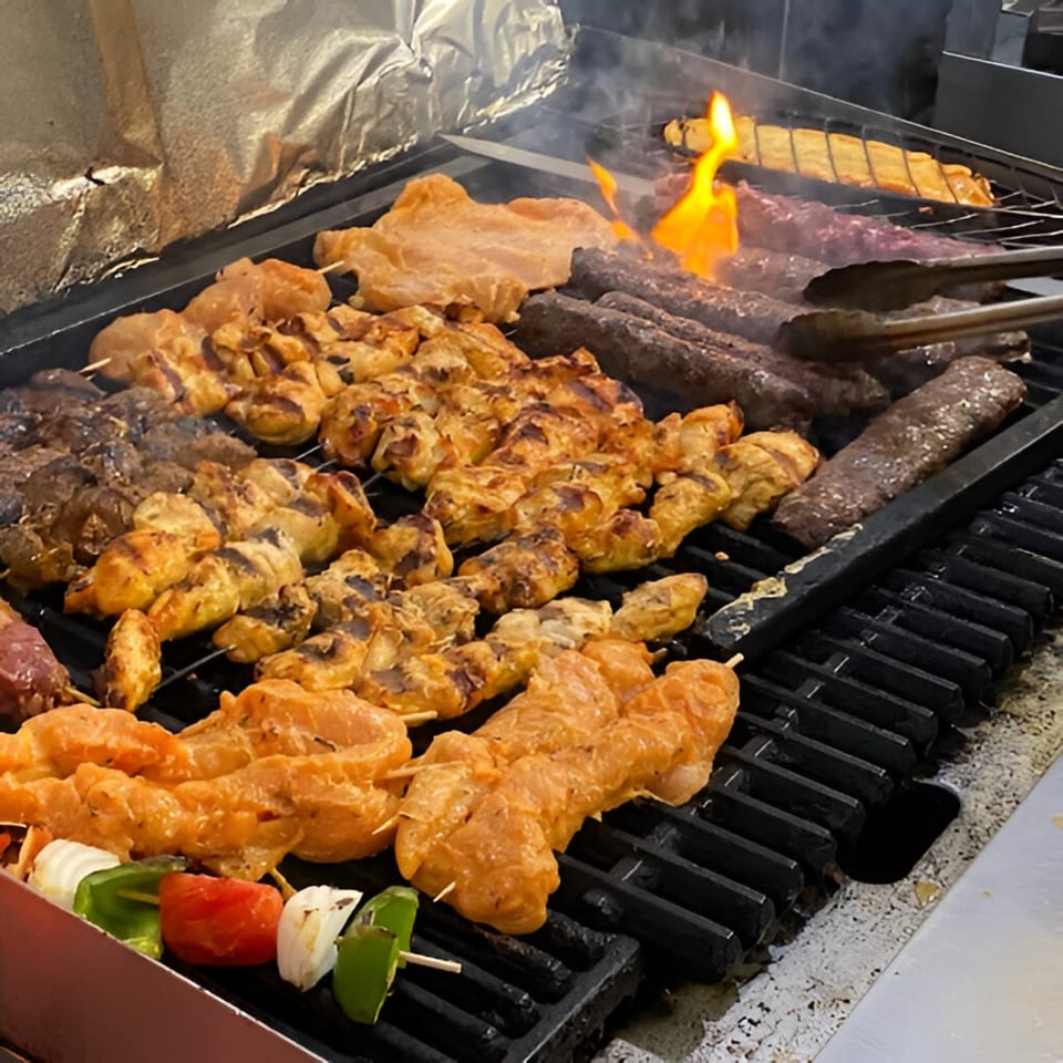 Various Mediterranean kabobs, including chicken, beef, and vegetable skewers, grilling over open flames.