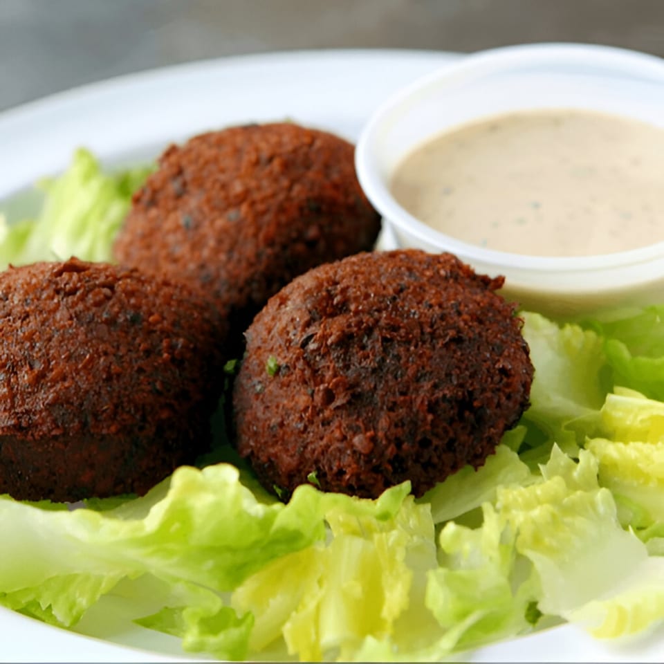 Three crispy falafel balls on a bed of fresh lettuce with a side of tahini sauce.