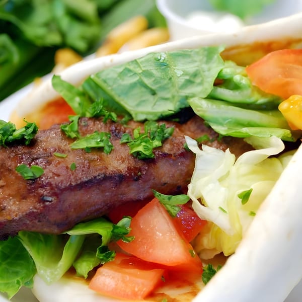 Close-up of a Mediterranean kabob wrap with grilled meat, fresh lettuce, and diced tomatoes.